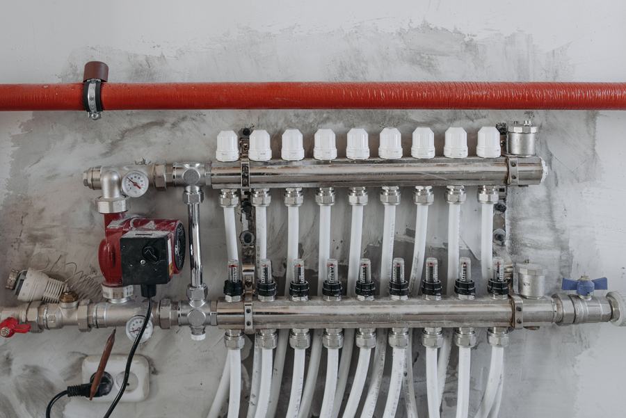 Collecteur de plancher chauffant avec ses vannes, sa pompe rouge et ses tuyaux blancs