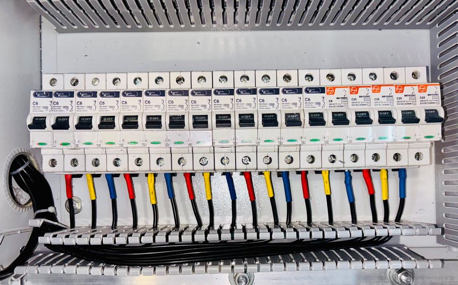 Tableau électrique ouvert avec une rangée de disjoncteurs modulaires et leurs fils colorés