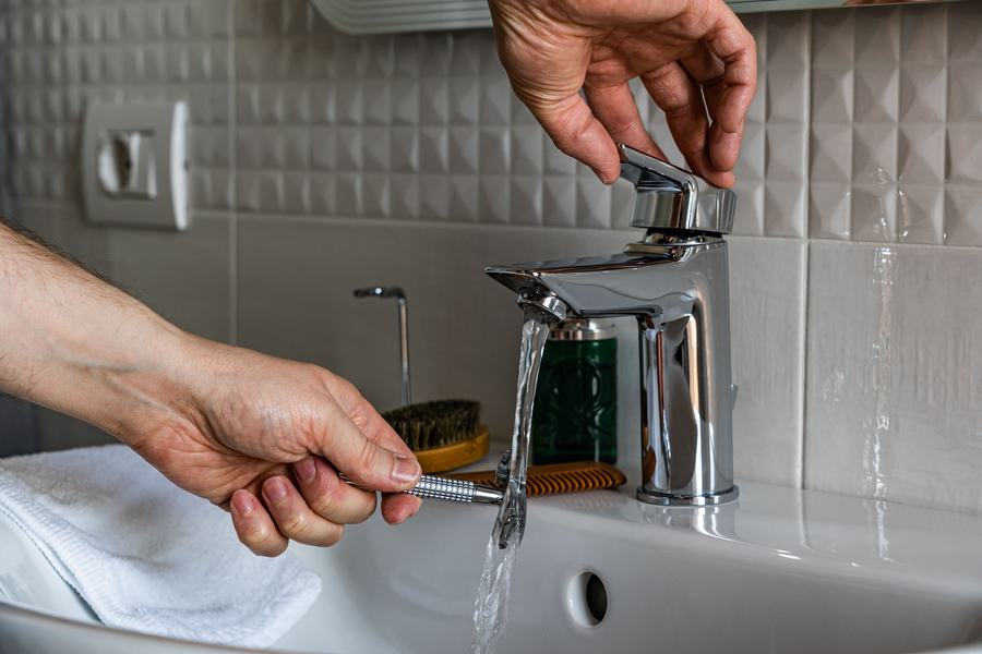 Main ouvrant un robinet chromé au-dessus d'un lavabo, avec un filet d'eau qui coule