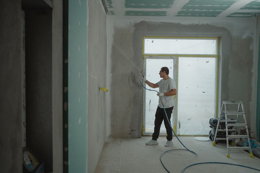 Pièce en rénovation aux murs lisses, dans laquelle un ouvrier peint à l'aide d'un pistolet